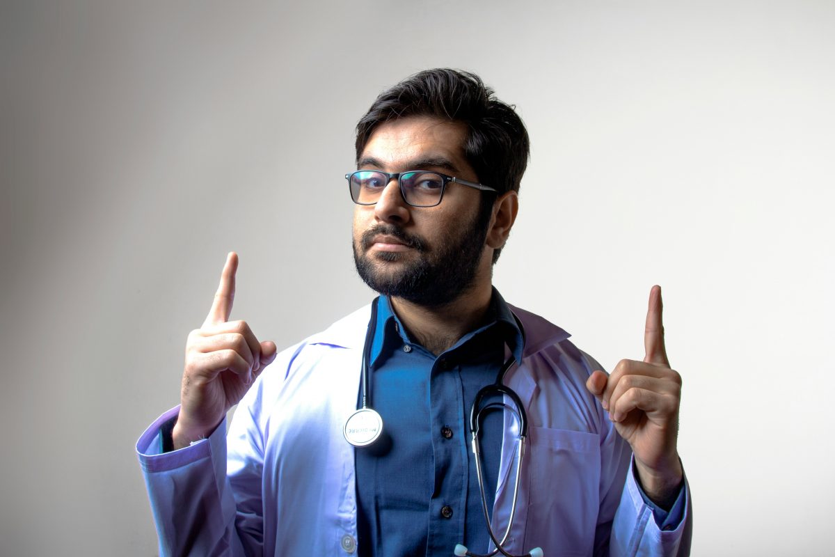 Confident male doctor in a white coat pointing upward, symbolizing the importance of choosing a qualified healthcare provider for penis enlargement surgery.